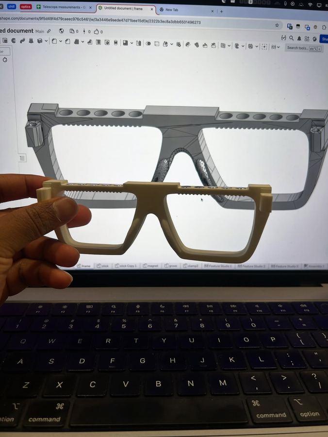 A printed frame held in front of a laptop with the CAD model