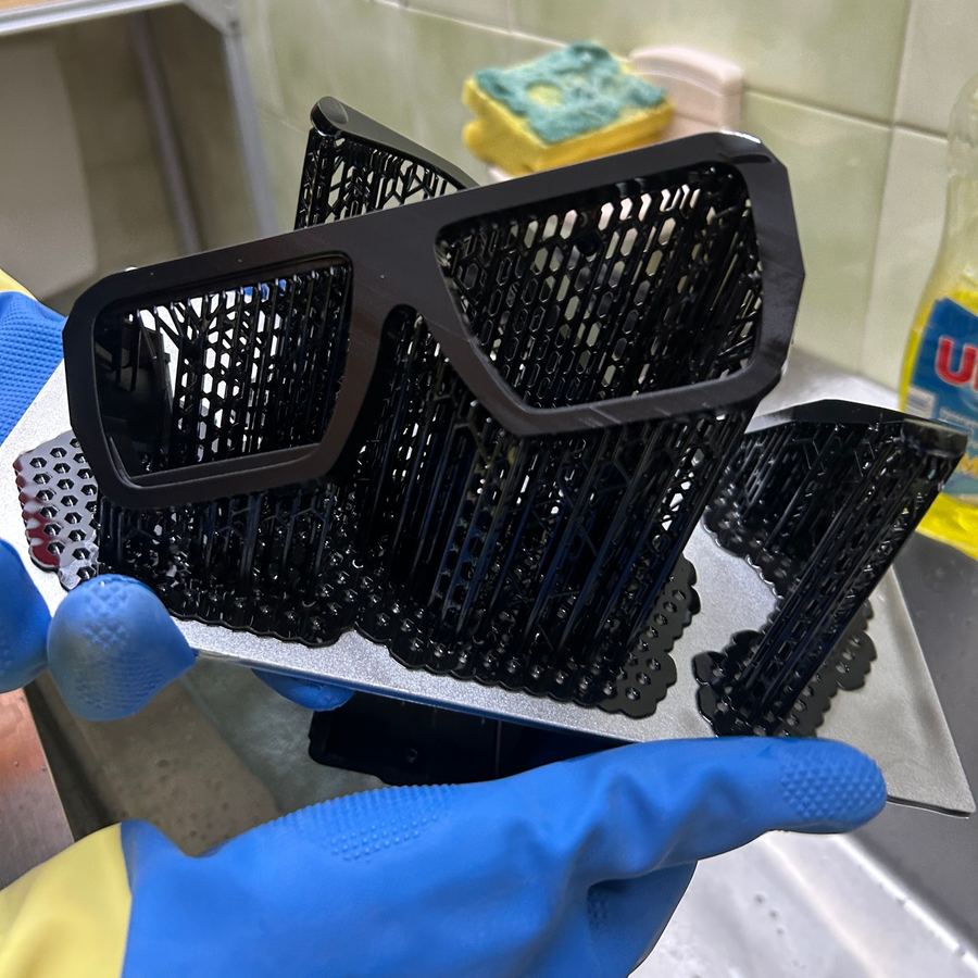 A resin printed frame covered in support structures, held in a gloved hand