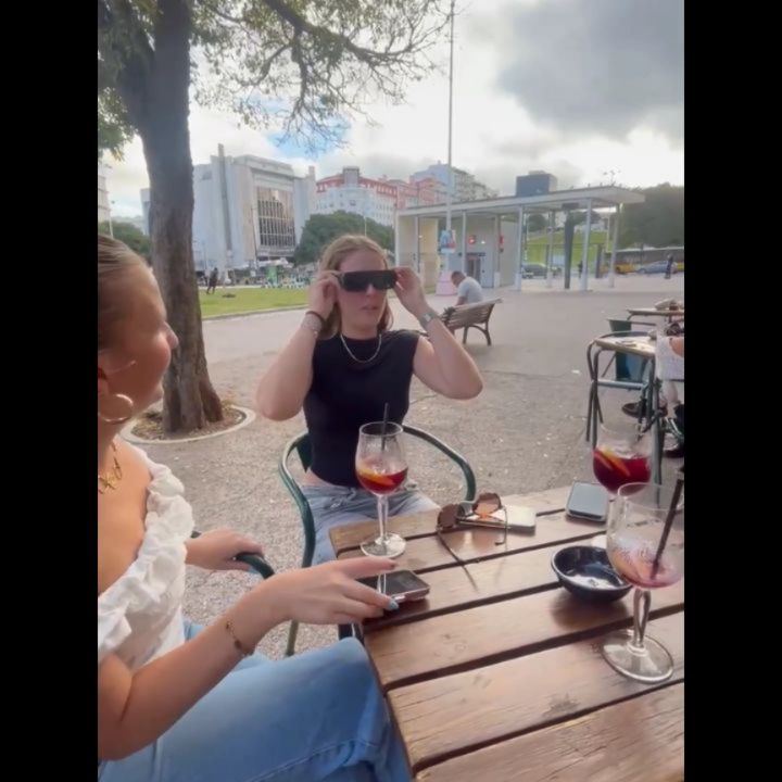 A woman at a café table wearing the glasses next to a friend