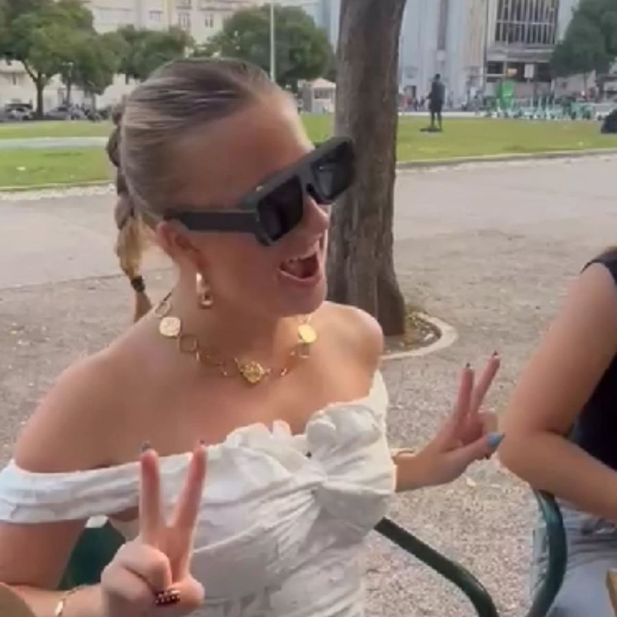 A woman in a white top making a peace sign in the glasses, outdoors