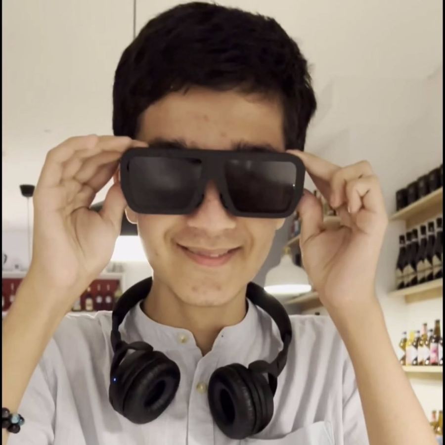 A teenager with headphones round his neck putting the glasses on